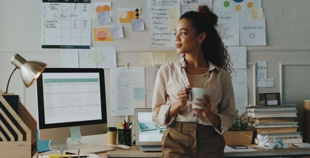 a woman holding a coffee mug smiling by her desk