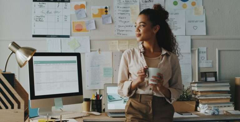 a woman holding a coffee mug smiling by her desk