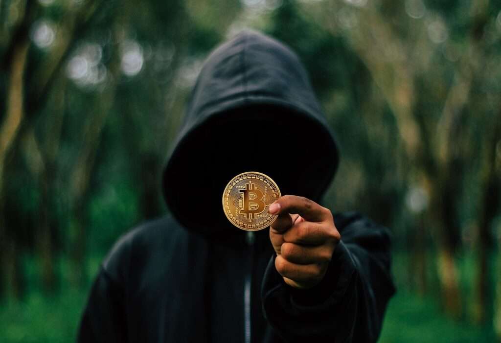 man in dark hood showing a btc coin