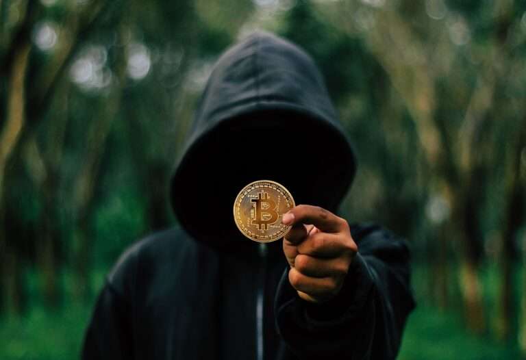 man in dark hood showing a btc coin