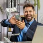 Cheerful rich Caucasian businessman boss working on laptop and wasting throwing money to camera more tips earnings big profit success win lottery shopping. Happy freelancer man guy at home office desk