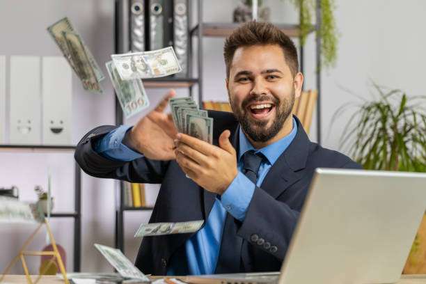 Cheerful rich Caucasian businessman boss working on laptop and wasting throwing money to camera more tips earnings big profit success win lottery shopping. Happy freelancer man guy at home office desk